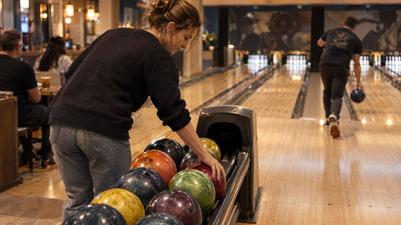 Frau wählt in einem Bowlingcenter eine Kugel vom Kugelrücklauf