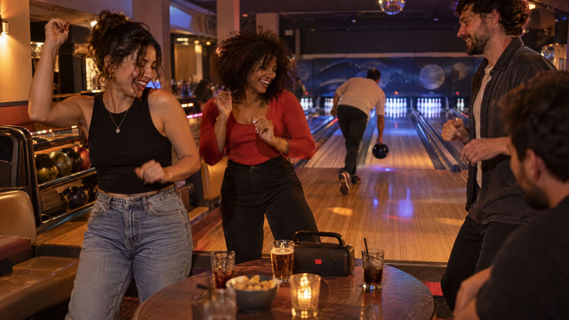 Venner danser og griner i siddeområdet, mens en bowler kaster