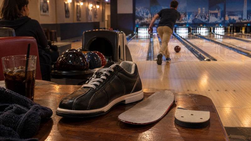 Black bowling shoe beside a removed slide sole and heel on a table in a bowling center