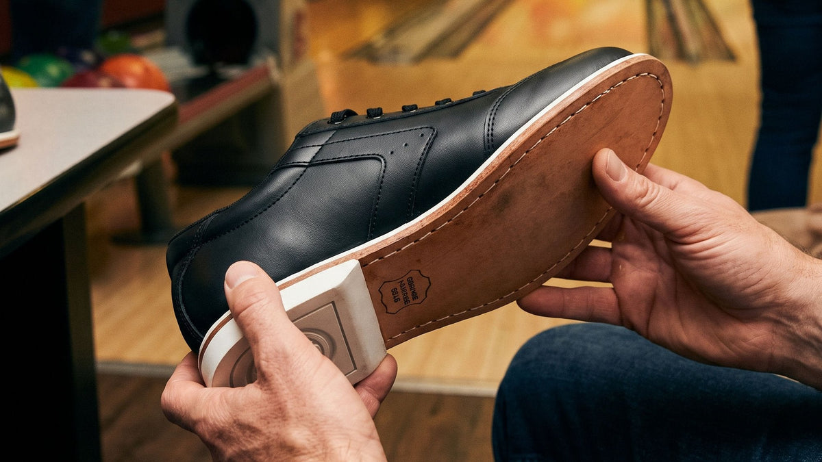Seated guest holding a black BOWLIO Nero bowling shoe, showing its leather sole and white heel