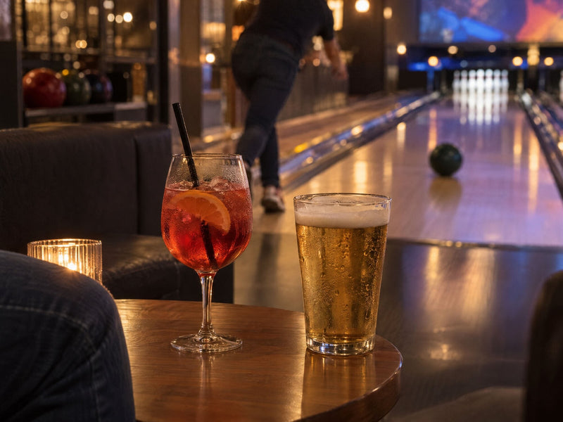 A spritz and a beer on a small table beside the lanes
