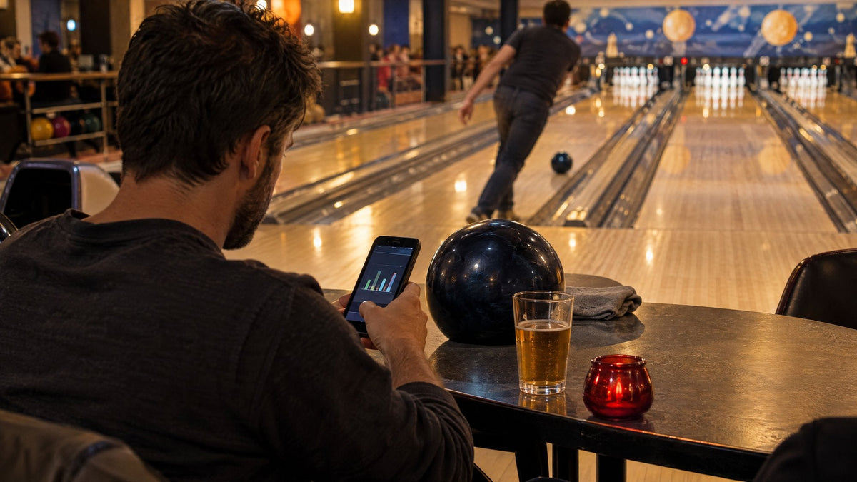 Bowler am Tisch schaut auf ein Diagramm auf seinem Smartphone, während ein anderer Bowler auf der Bahn wirft