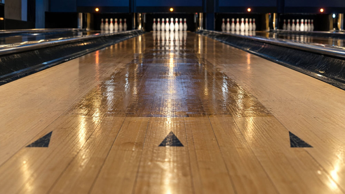 Oil glistening on the middle boards of a wooden bowling lane, with the aiming arrows in front