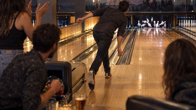 Friends cheering as the pins fly at the end of the lane after a bowler's shot